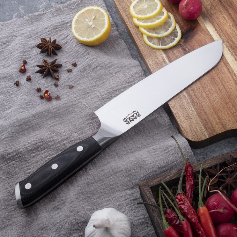 Couteau Santoku Sanakaza posé sur un linge en lin gris avec des tranches de citron, des piments rouges frais, de l'ail et des étoiles d'anis.