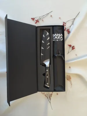 Coffret cadeau cuisine Sanakaza ouvert contenant le couteau Santoku 18 cm avec son étui et le tablier noir plié dans son alvéole.