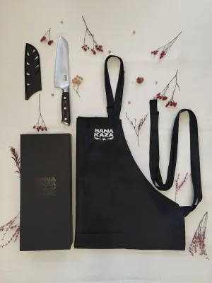 Coffret cadeau Sanakaza ouvert contenant le couteau Santoku 18 cm avec son étui et le tablier noir plié dans son alvéole.