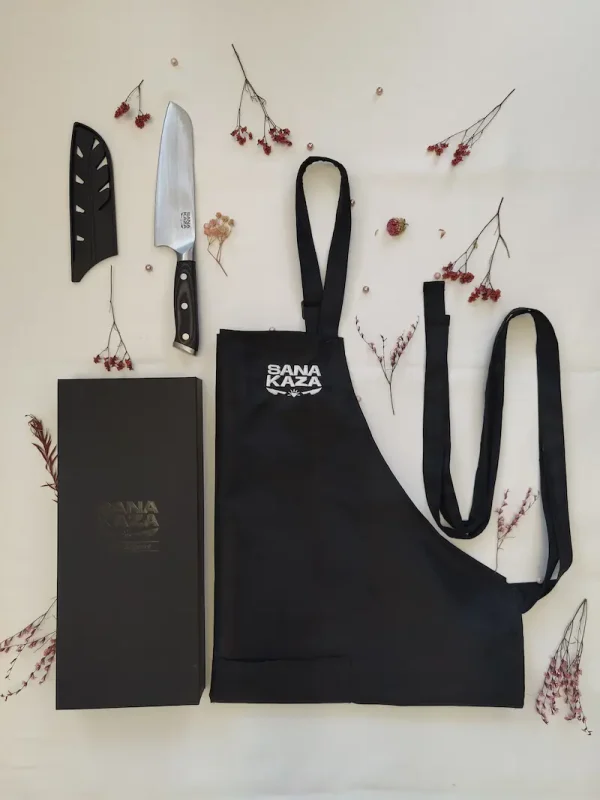 Coffret cadeau Sanakaza ouvert contenant le couteau Santoku 18 cm avec son étui et le tablier noir plié dans son alvéole.